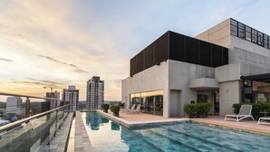 A rooftop swimming pool with lounge chairs, a glass railing, and a view of surrounding buildings. - The Hub Urban Hotel (Asunción)