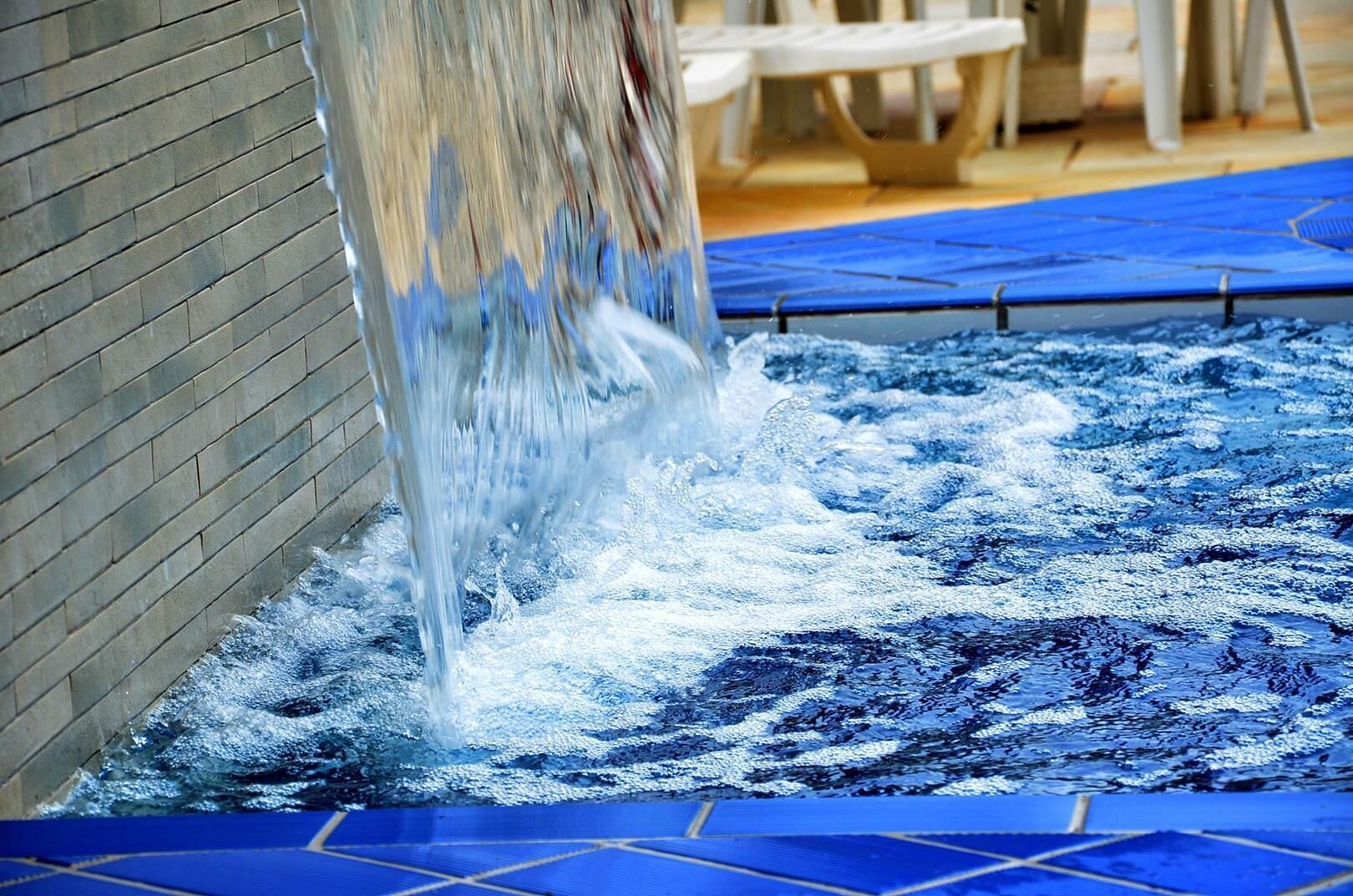 Uma fonte com fluxo em cascata para uma piscina com azulejos azuis.