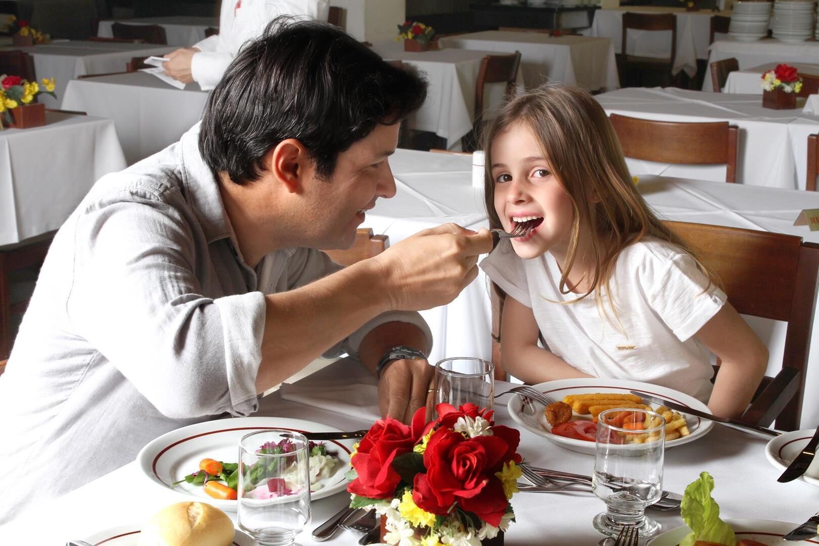 A dining table with plates of food, a glass of water, and a vase of red roses.
