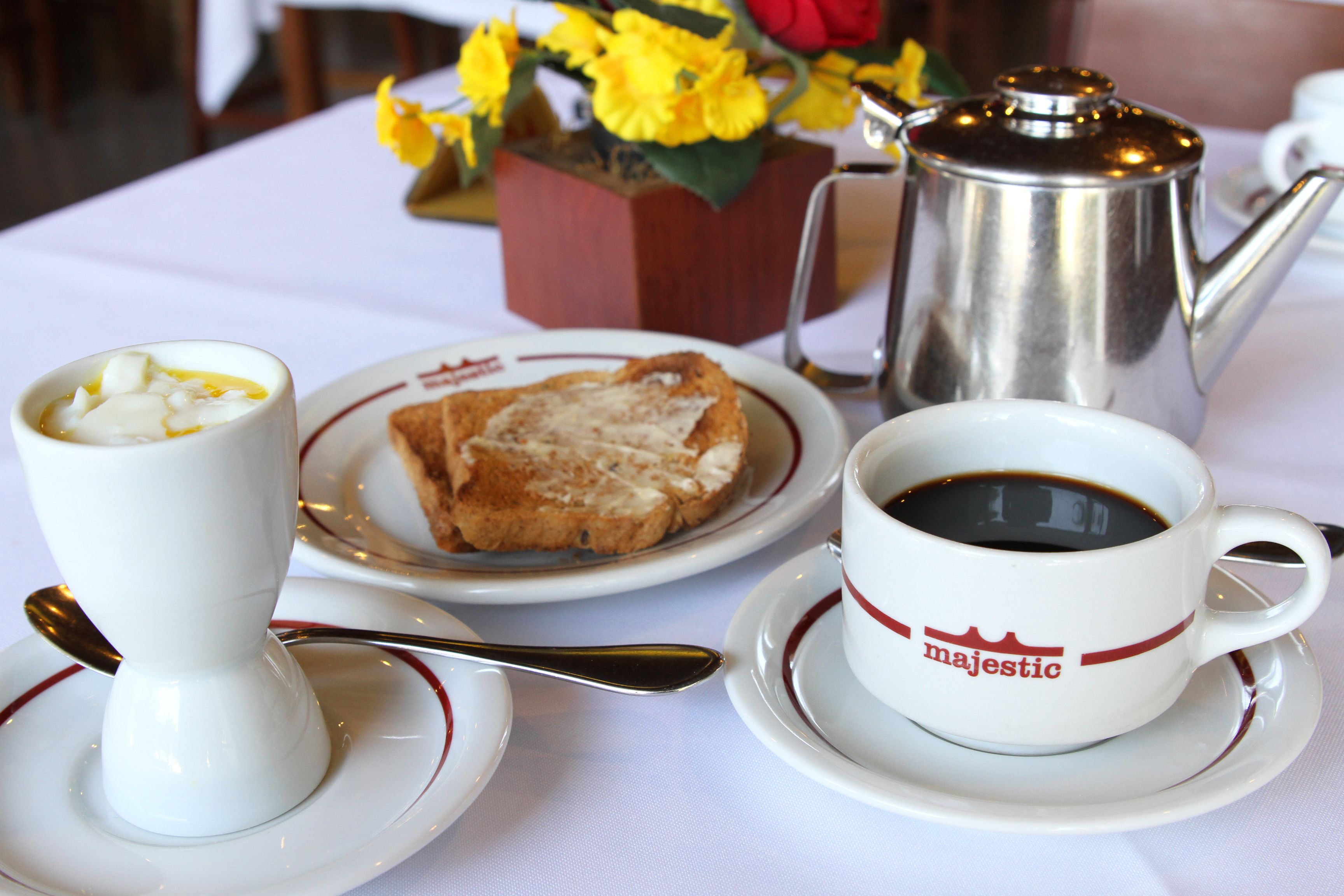 A breakfast setting with a cup of coffee, toast, and a teapot on a table.