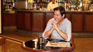Un hombre sentado a una mesa redonda en la zona de bar, con una taza de café y un menú frente a él.