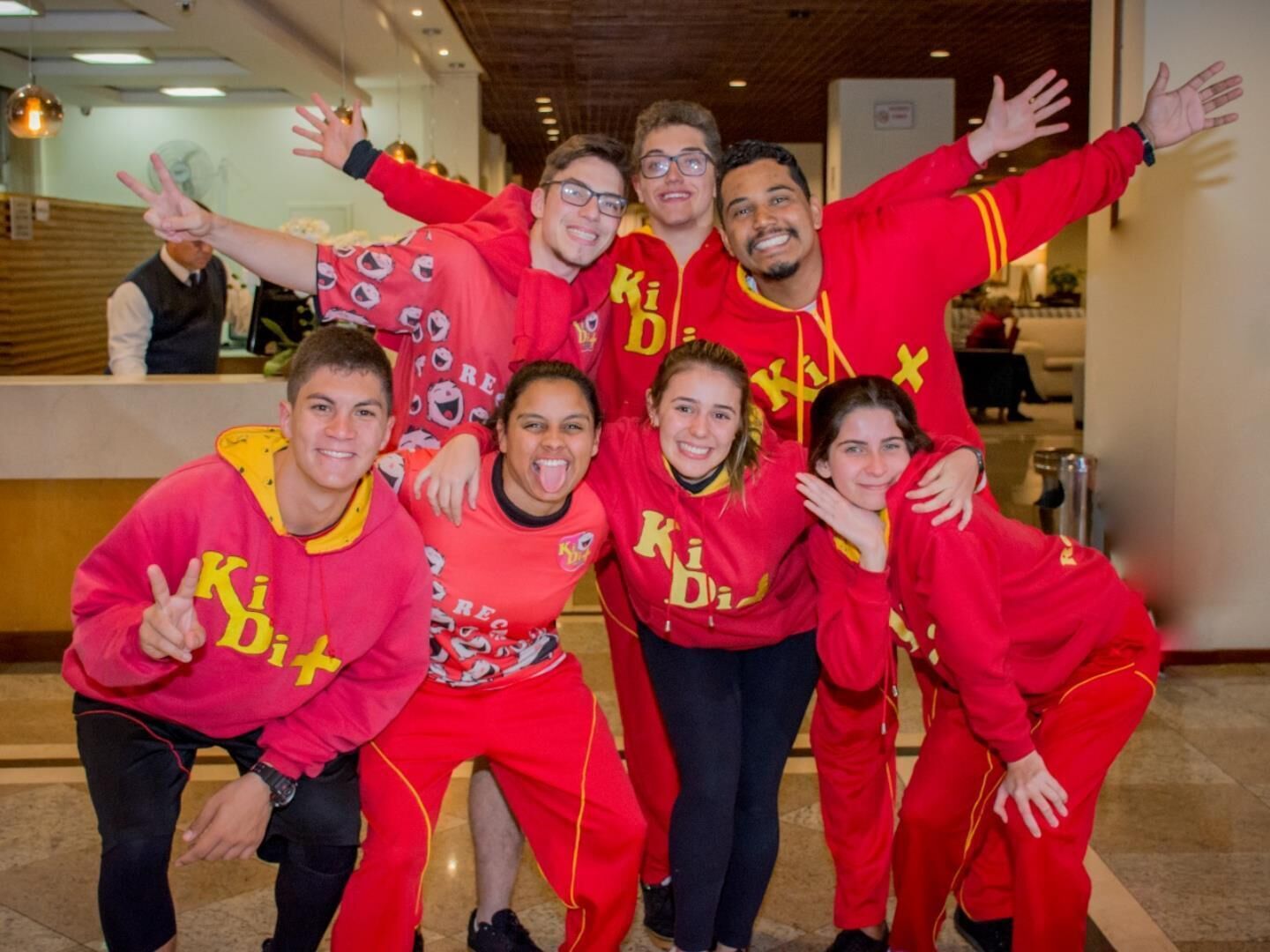 A group of people in red uniforms posing for a photo in a lobby with a wooden ceiling and a reception desk in the background.