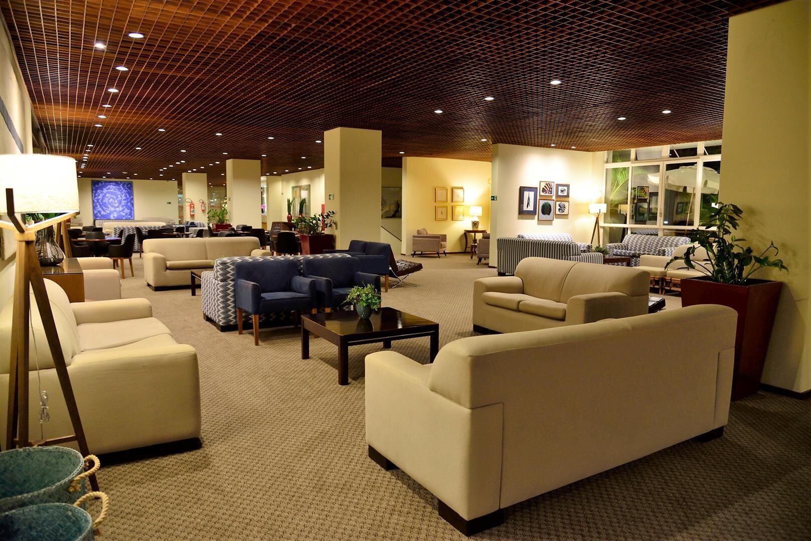 Een ruime lobby met meerdere zithoeken, waaronder banken en fauteuils, gerangschikt rond een centrale salontafel. Het plafond heeft een houten rasterontwerp, en de muren zijn versierd met ingelijste kunstwerken.