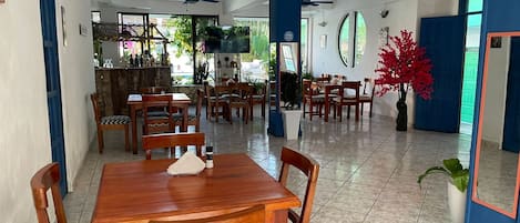 A spacious dining area with wooden tables and chairs, a bar area with a TV, and a large mirror on the wall.
