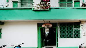 Un edificio de varios pisos con fachada verde, unidades de aire acondicionado y un letrero que indica que es un hotel.
