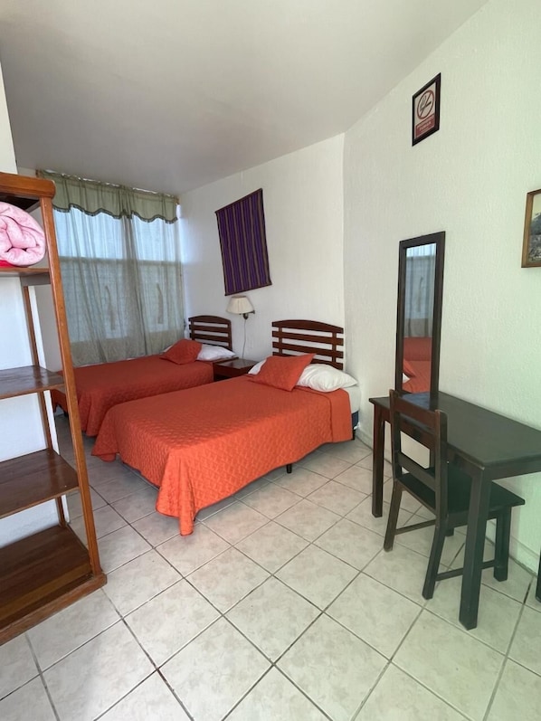 Una habitación con dos camas, un escritorio y una silla. Cuenta con una ventana con cortinas y una lámpara de pared.