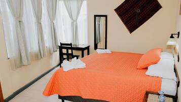 A neatly made bed with an orange bedspread, a bedside table with a lamp, and a chair.