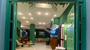 La entrada del Hotel Sabana, con una zona de recepción, asientos y una decoración en tonos verdes.