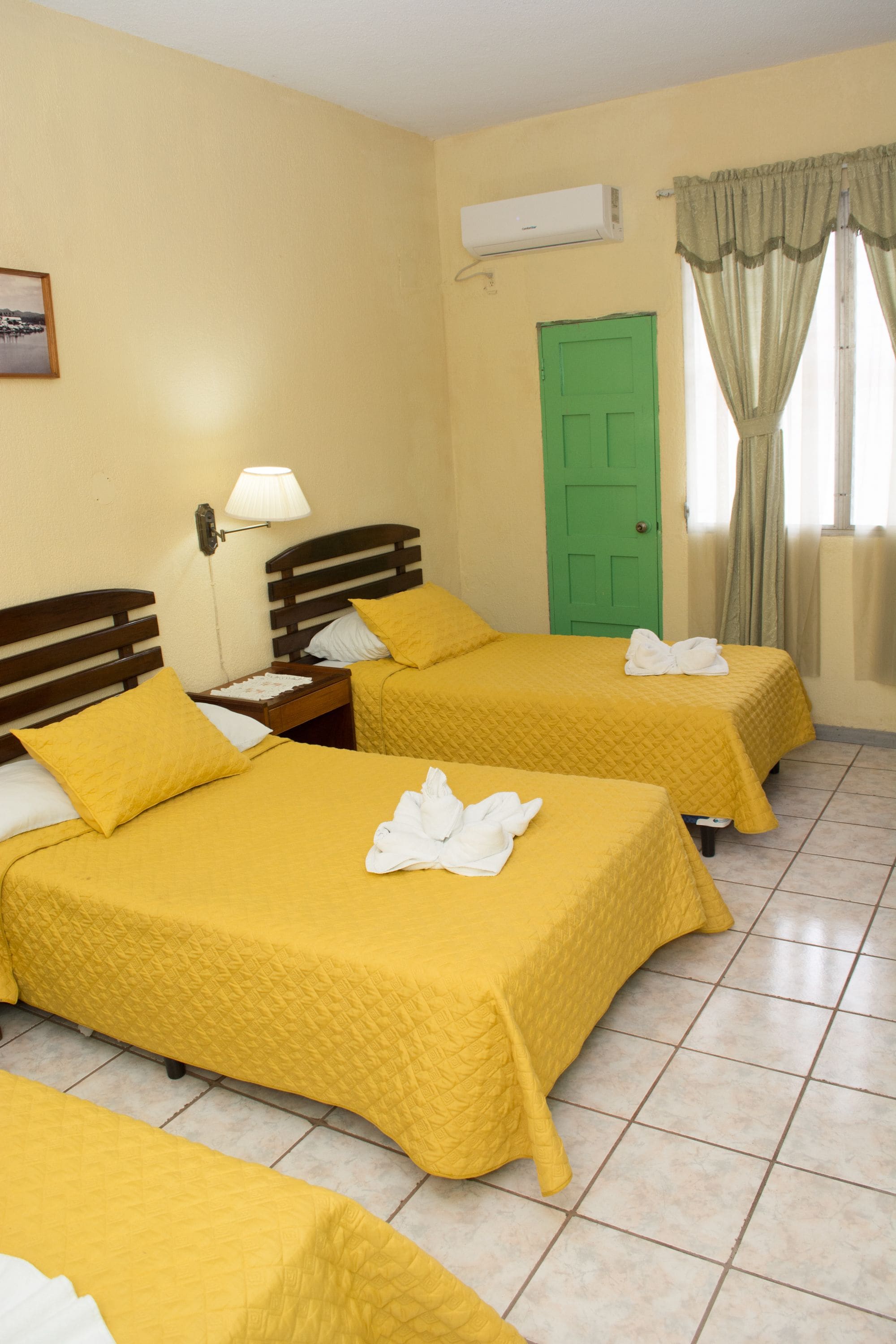 A hotel room with two beds, a green door, and a window with curtains.
