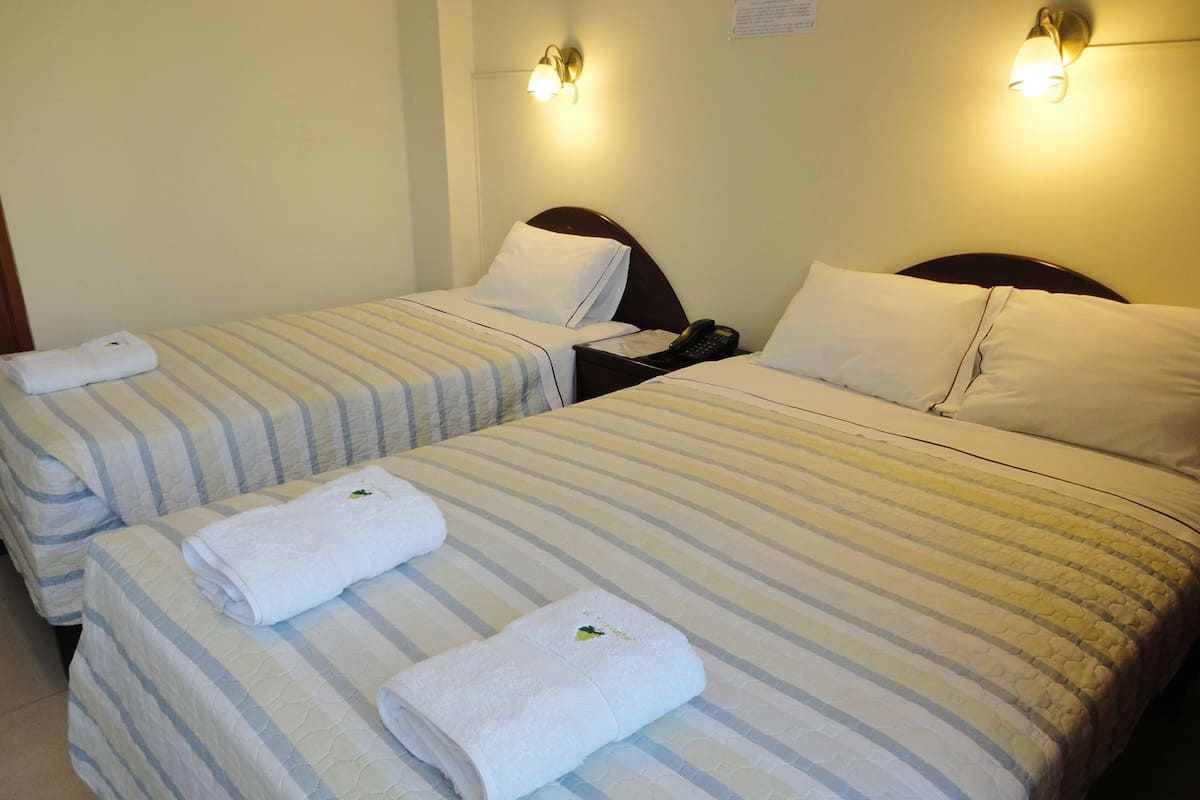 A hotel room with two beds, each with striped bedding and white pillows. There are two bedside lamps and a telephone on the nightstand.