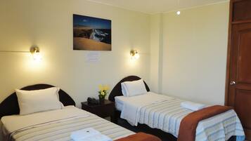 Quarto de hotel com duas camas, uma mesa de cabeceira, um quadro de uma cena de praia e uma porta.