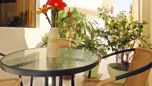 Une table ronde en verre, surmontée d’un vase tressé et agrémentée de plantes en pot, entourée de chaises en osier.