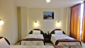 Une chambre d’hôtel avec deux lits, une table de chevet avec un téléphone, un tableau au mur et une fenêtre avec des rideaux.