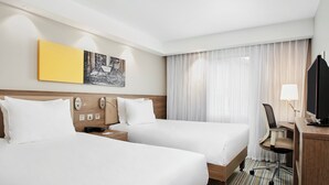 A hotel room with two beds, a desk with a chair, a television, and a window with curtains. - Hampton by Hilton Oxford (Oxford)