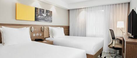 A hotel room with two beds, a desk with a chair, a television, and a window with curtains.