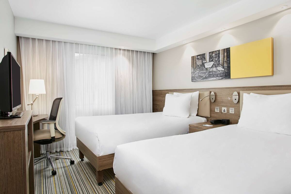 Una habitación de hotel con dos camas, un escritorio con televisor, una silla y una lámpara.