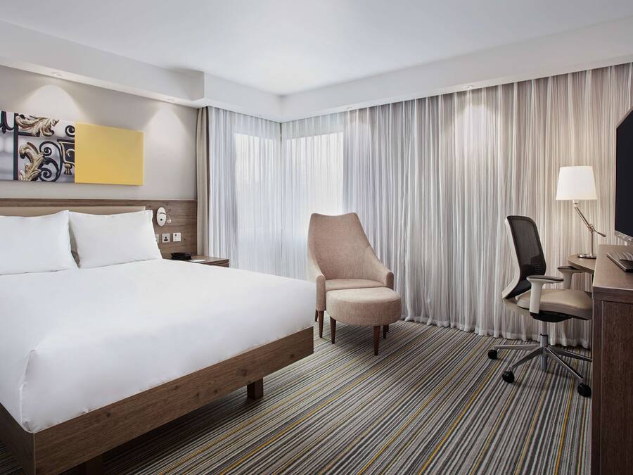 A hotel room with a large bed, a desk with a computer, a chair, and a television.