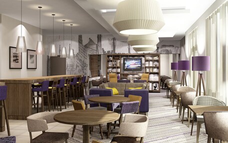 A modern hotel lobby with multiple seating areas, a television, and a bar.