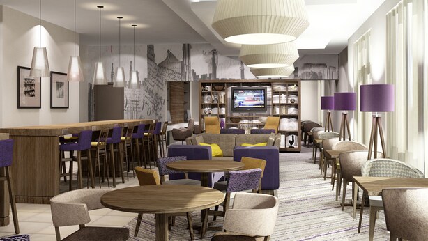 A modern hotel lobby with multiple seating areas, a television, and a bar. - Hampton by Hilton Oxford (Oxford)