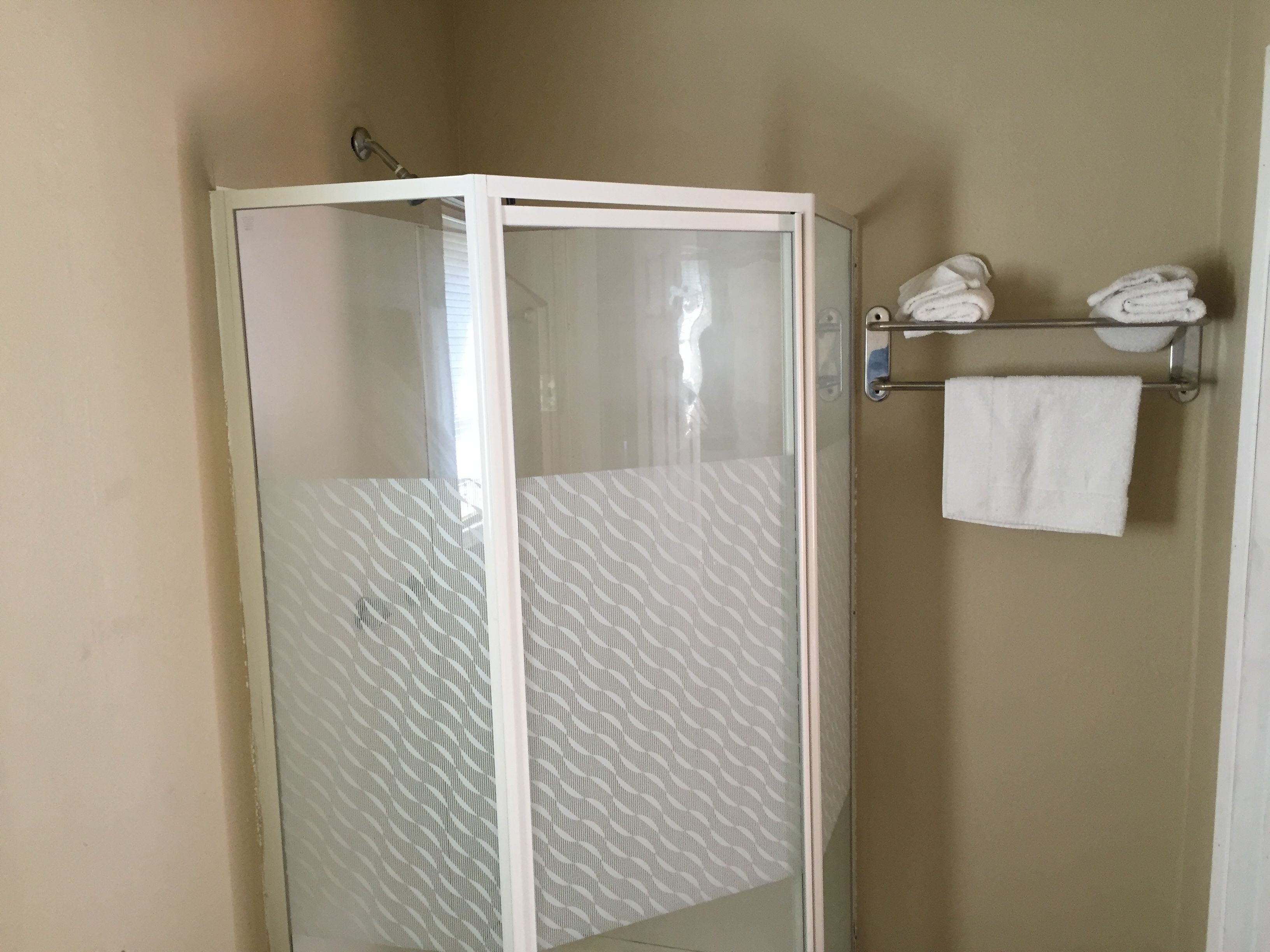 A shower area with a glass door, a towel rack with folded towels, and a plain wall.