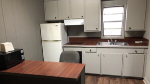 A compact kitchen with white cabinets, a refrigerator, a microwave, and a wooden table. - Morgan City Motel (Morgan City)