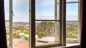 A room with a large window overlooking a cityscape, a wooden desk, and a metal chair. - Kiwi Heritage Homestay (Auckland)