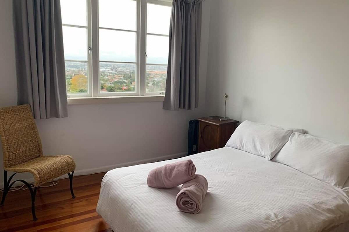 Ein Schlafzimmer mit einem Bett, einem Sessel, einem Nachttisch und einem Fenster mit Vorhängen.