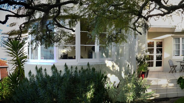 A modern house with a covered patio, large windows, and lush greenery. - Kiwi Heritage Homestay (Auckland)