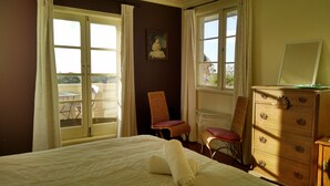 A bedroom with a bed, two wicker chairs, a wooden dresser, and a painting on the wall. - Kiwi Heritage Homestay (Auckland)