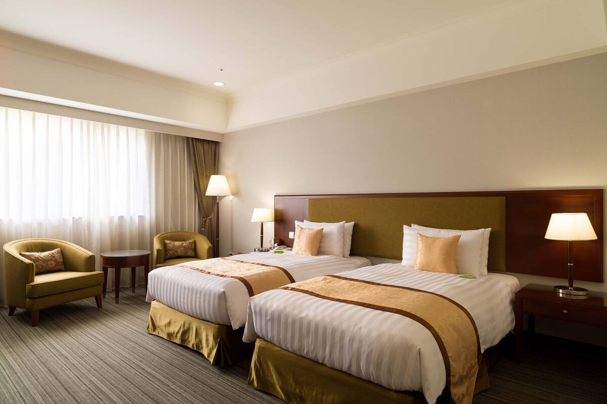 Une chambre d’hôtel avec deux lits, un canapé, une petite table et une lampe.