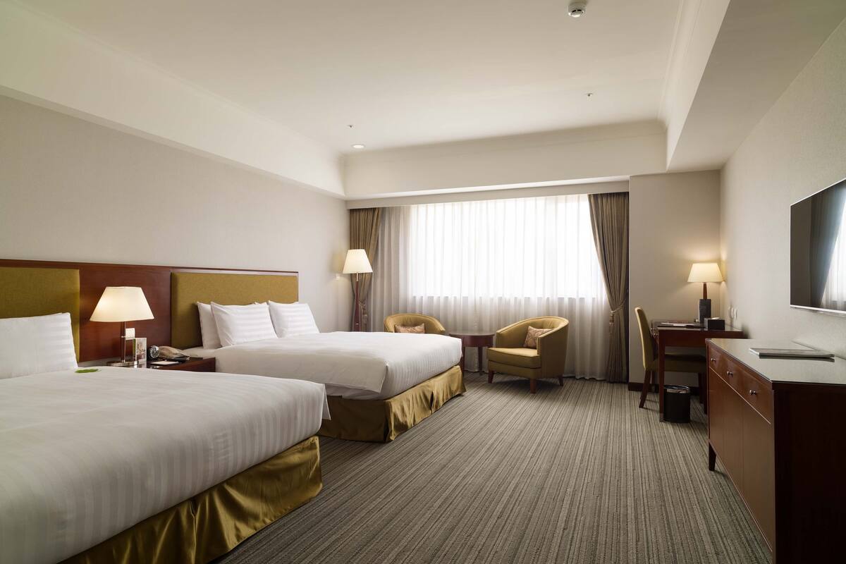 Une chambre d’hôtel avec deux lits, un bureau, une chaise, une télévision et une fenêtre avec des rideaux.