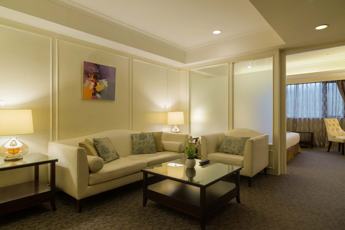 Une chambre d’hôtel avec un canapé beige, une table basse en verre, une lampe et un tableau au mur.
