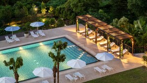 A pool area with lounge chairs and umbrellas, surrounded by lush greenery and overlooking a body of water with buildings in the background. - The Grand Hotel Kaohsiung (Kaohsiung)
