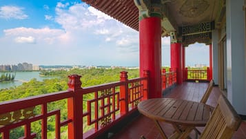 A balcony with a view of a lake and cityscape, featuring red railings and a wooden table.