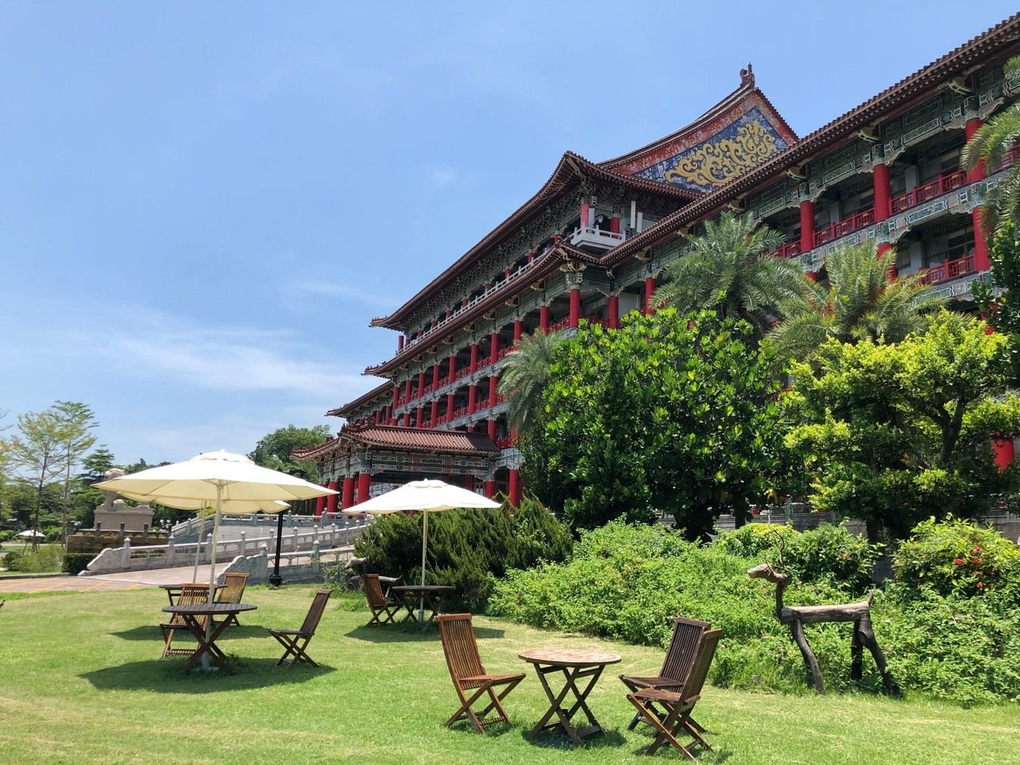 A traditional building with a multi-tiered roof and red columns, surrounded by a well-maintained garden with outdoor seating.