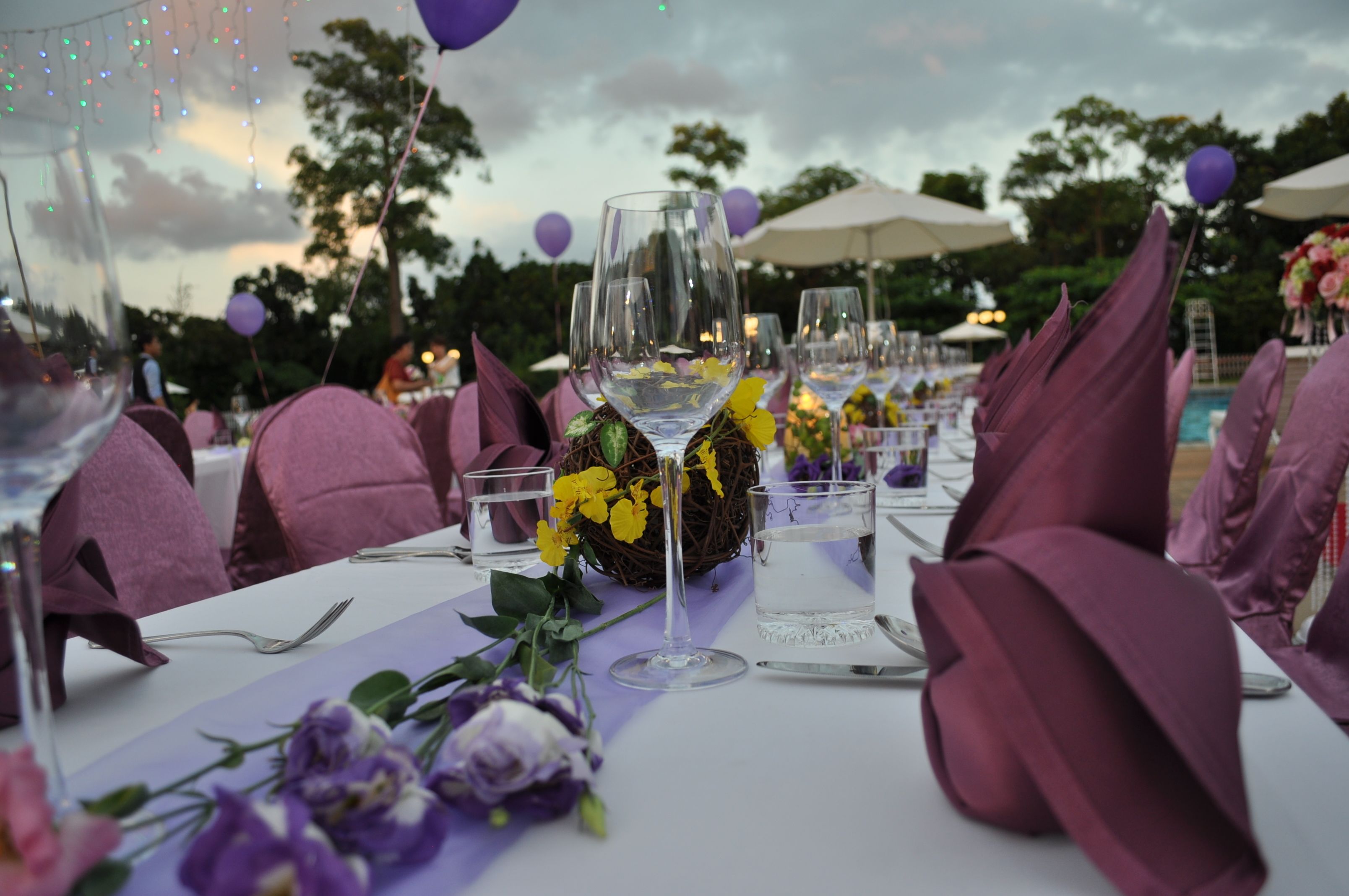 A table set with purple napkins, clear glasses, and yellow flowers.