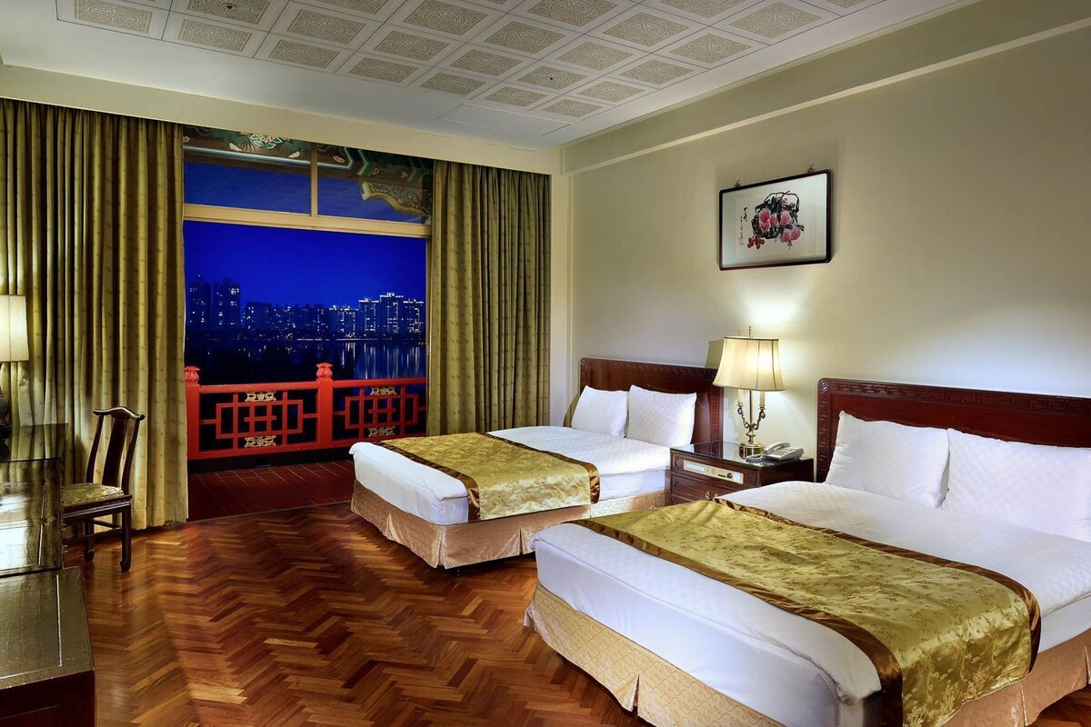 A hotel room with two beds, a city view, a balcony, and a wooden floor.