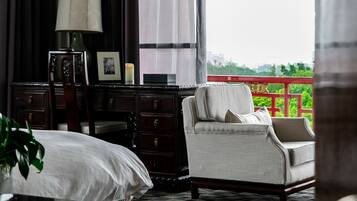 Habitación de hotel con cama, una silla, un escritorio y un ventanal con vistas a zonas verdes y un edificio.