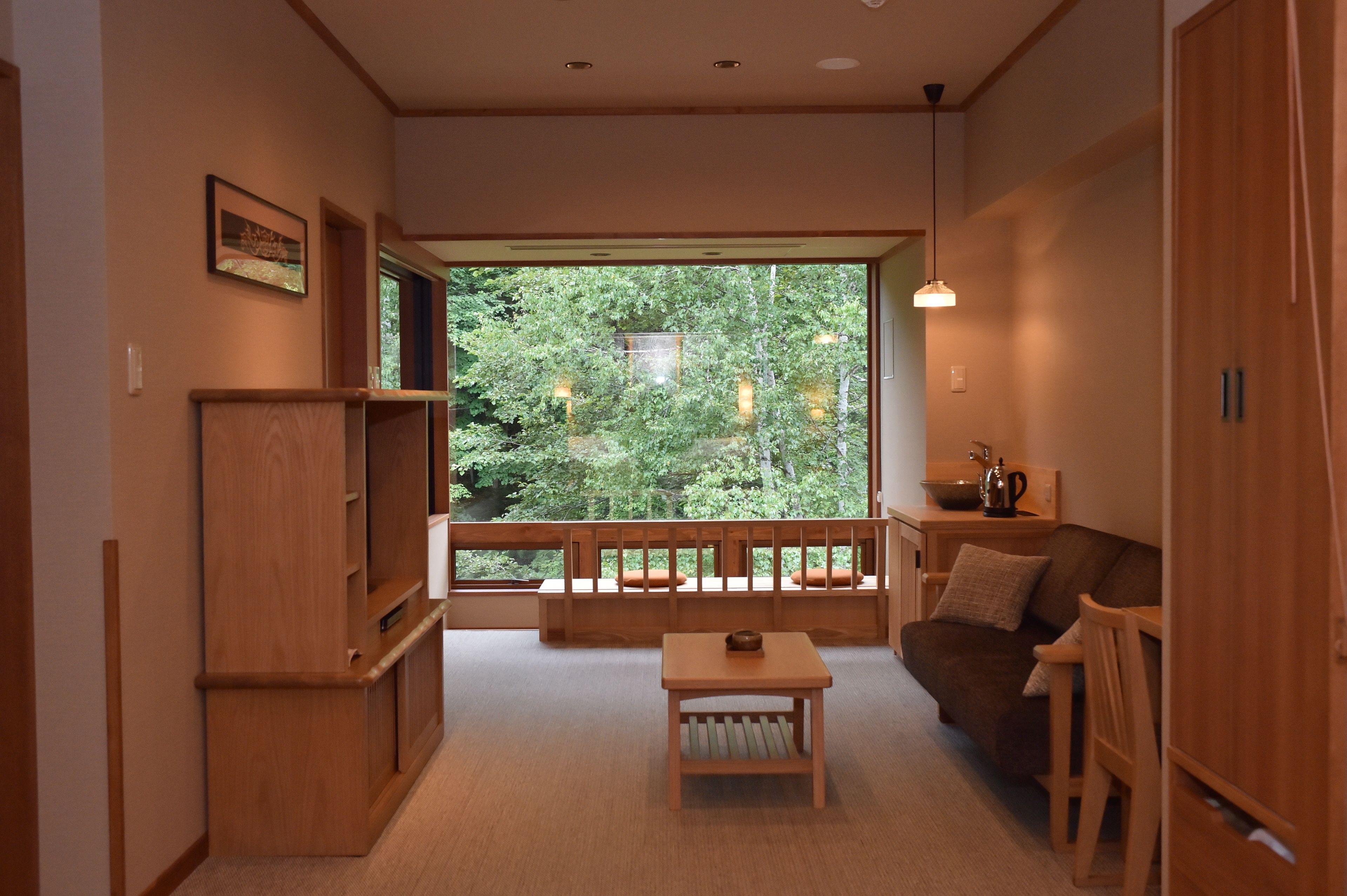 A cozy living room with a large window, wooden furniture, and a view of greenery outside.