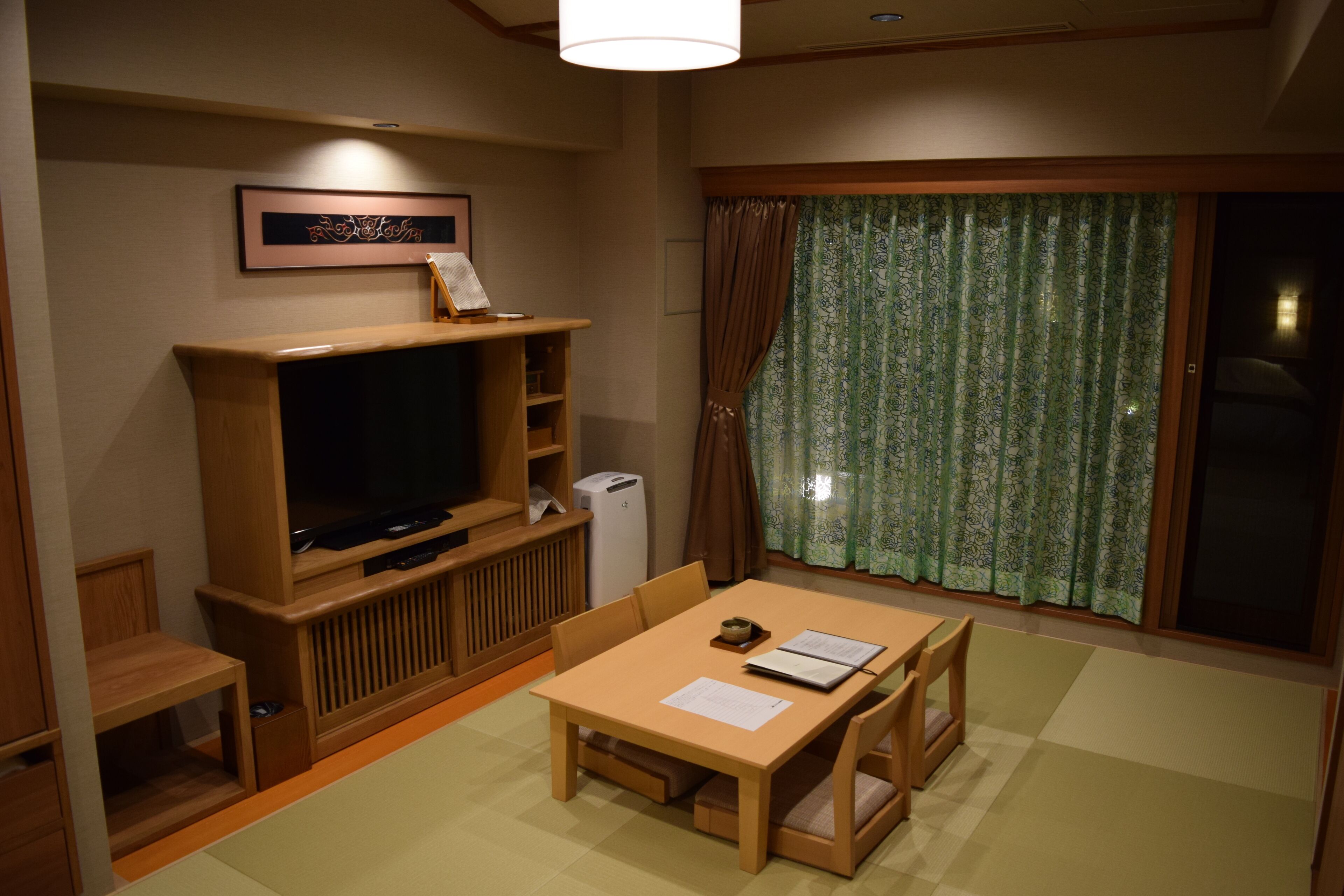 Een woonkamer met een televisie, houten meubels, een klein tafeltje en een raam met gordijnen.