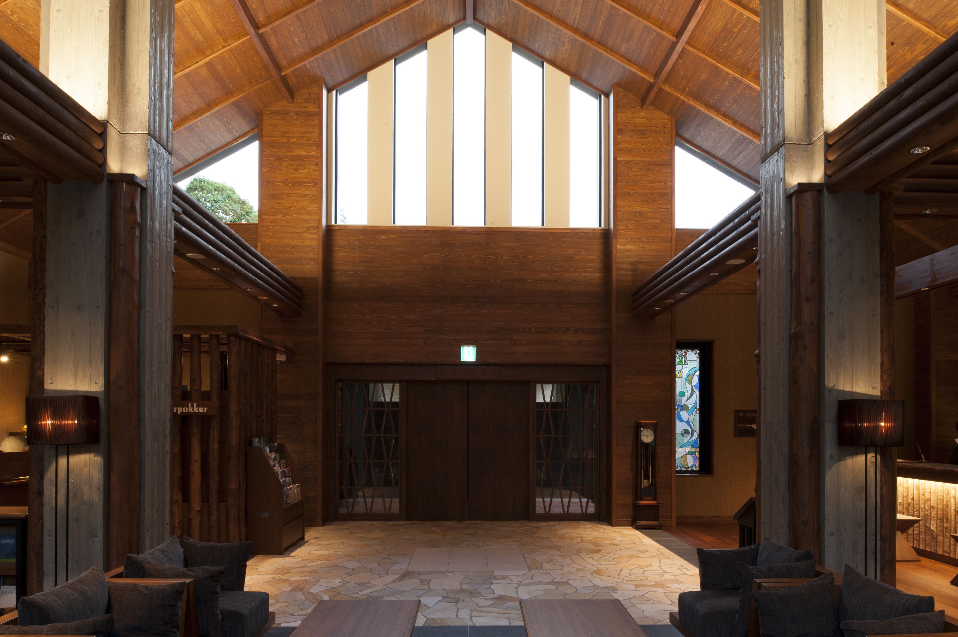 A spacious lobby with a high ceiling, large wooden doors, and a stone floor.