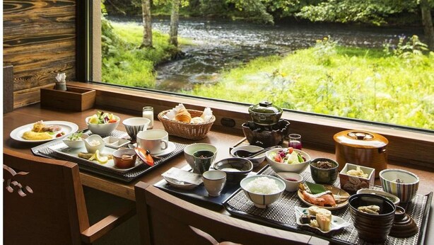A dining table with various dishes and tea set, overlooking a river and greenery. - La Vista Akangawa - Adults only (Kushiro)