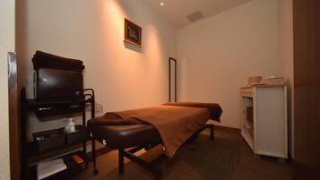 A room with a massage table, a TV on a stand, a small cabinet, and a wall-mounted picture.