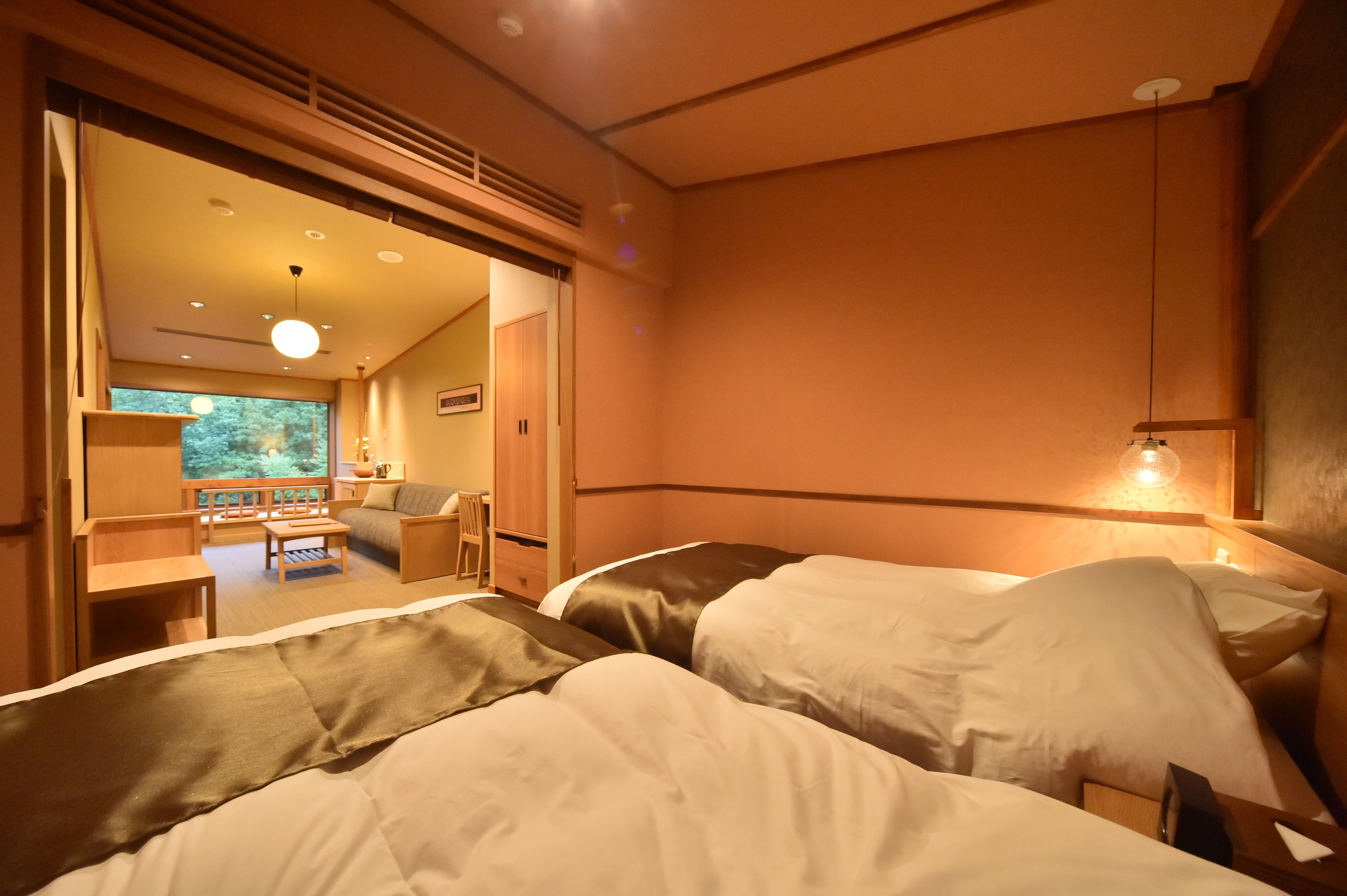 A hotel room with two beds, a wooden desk, a chair, and a large window.