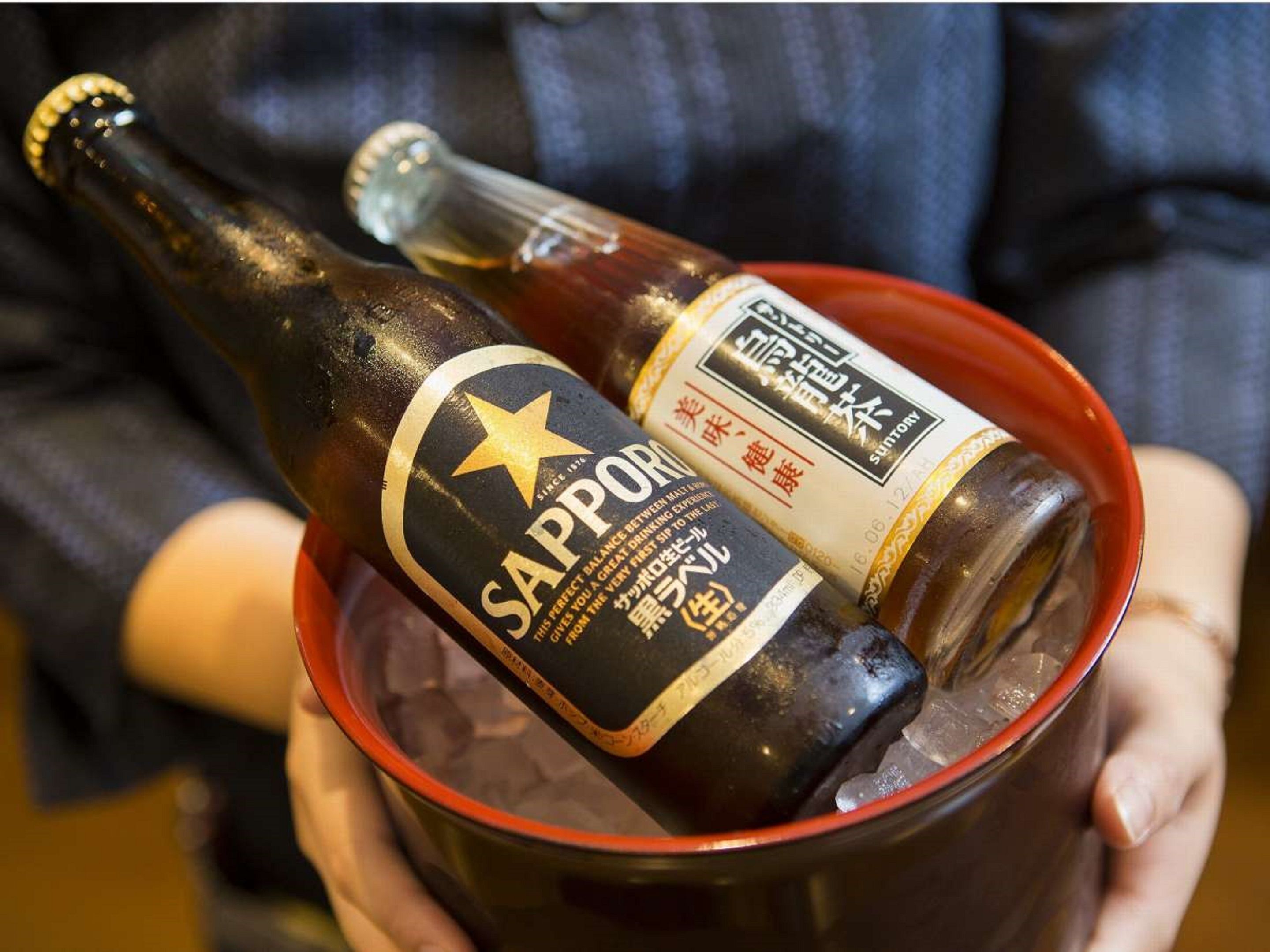 Una persona sosteniendo una botella de cerveza Sapporo en un cubo.