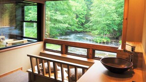 A room with a large window overlooking a forested area with a stream. There is a wooden bench and a sink with a bowl. - La Vista Akangawa - Adults only (Kushiro)