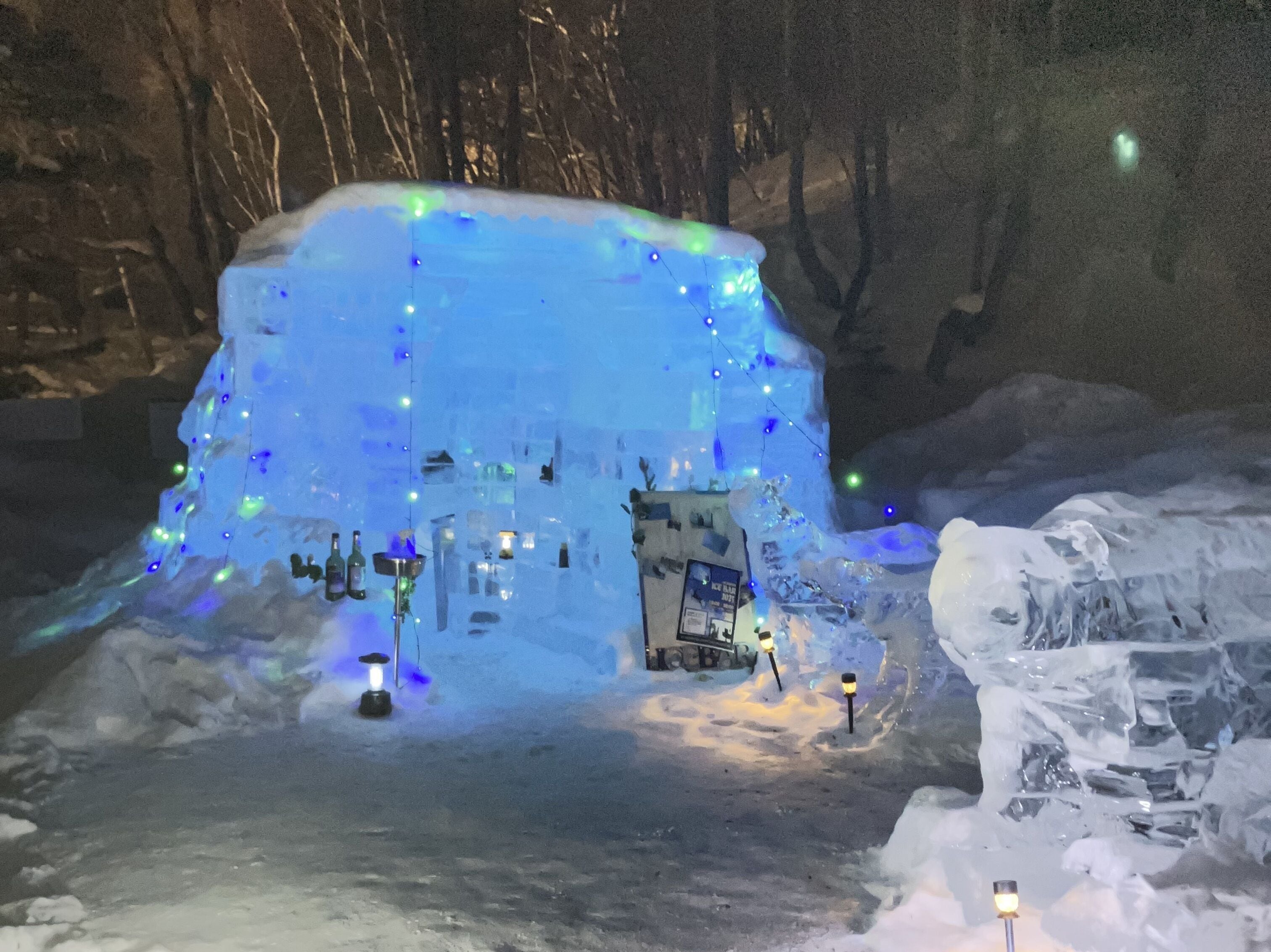 Une structure de glace agrémentée de lumières intégrées et surmontée d’un petit bâtiment, le tout étant entouré de neige.