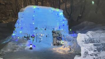 Une structure de glace agrémentée de lumières intégrées et surmontée d’un petit bâtiment, le tout étant entouré de neige.