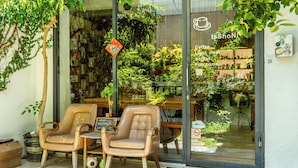 Un café con dos sillones de cuero en el exterior, una puerta de cristal con el menú y una pequeña zona de estar al aire libre.