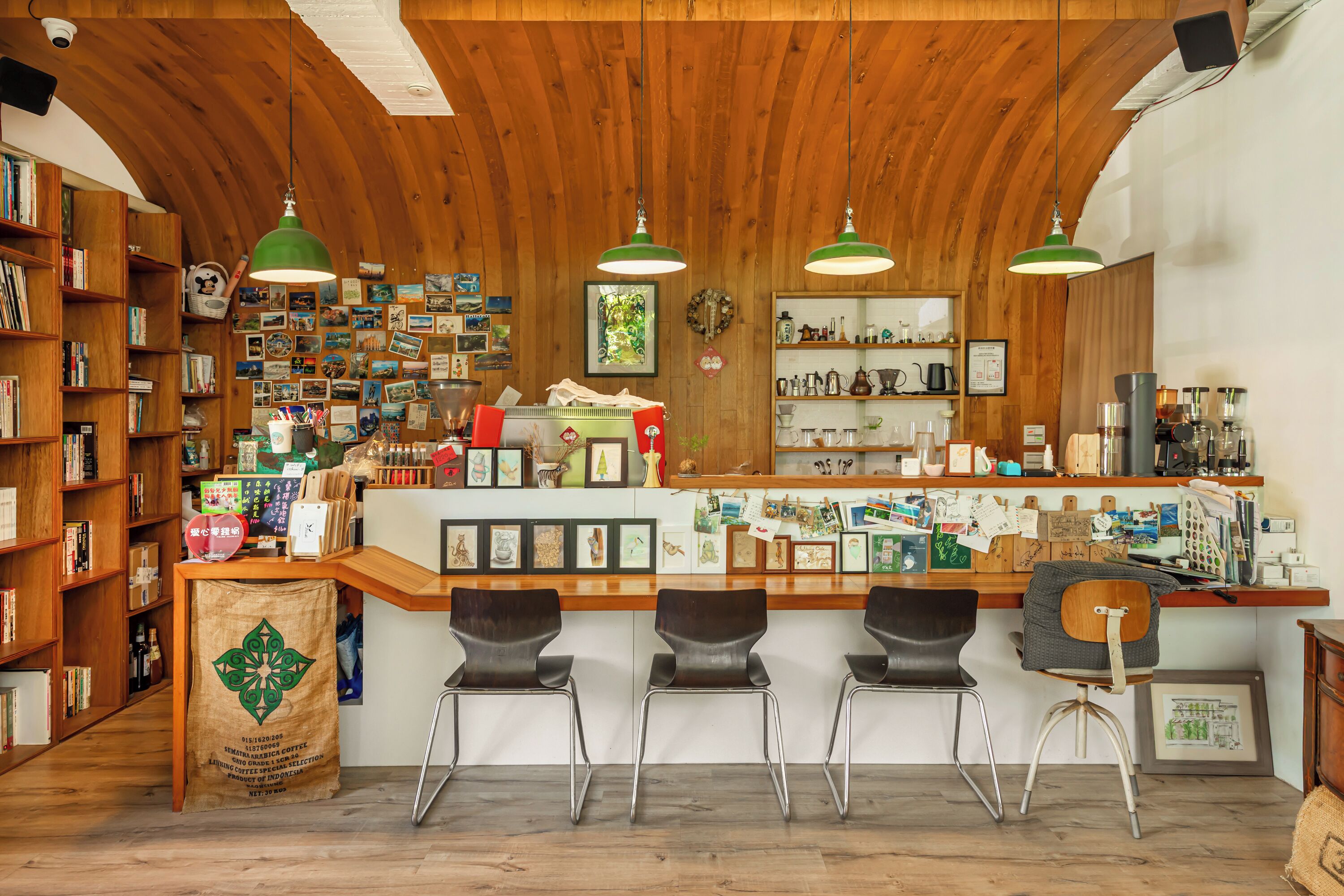 Un café chaleureux aux murs en bois, avec un comptoir et des tabourets, et des étagères remplies de livres et d'accessoires pour préparer le café.